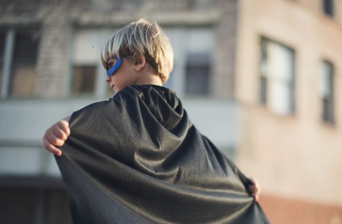 auf dem Bild zu sehen ist ein kleiner Junge mit Superheldenmaske, der hinter sich ein Cape ausbreitet.