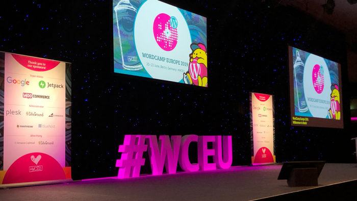 Zu sehen ist die Bühne des WordCamp Europe 2019 mit diversen Begrüßungstexten auf den Leinwänden