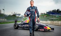 Zu sehen ist Davis Coulthard vor einem Rennwagen mit Helm unterm Arm